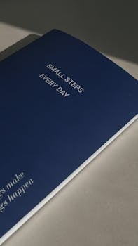 Blue notebook cover with motivational text 'Small Steps Every Day' in minimal light.