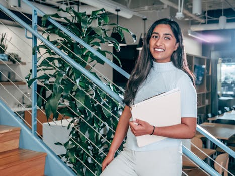 Young female professional smiling and holding documents in a modern office setting.